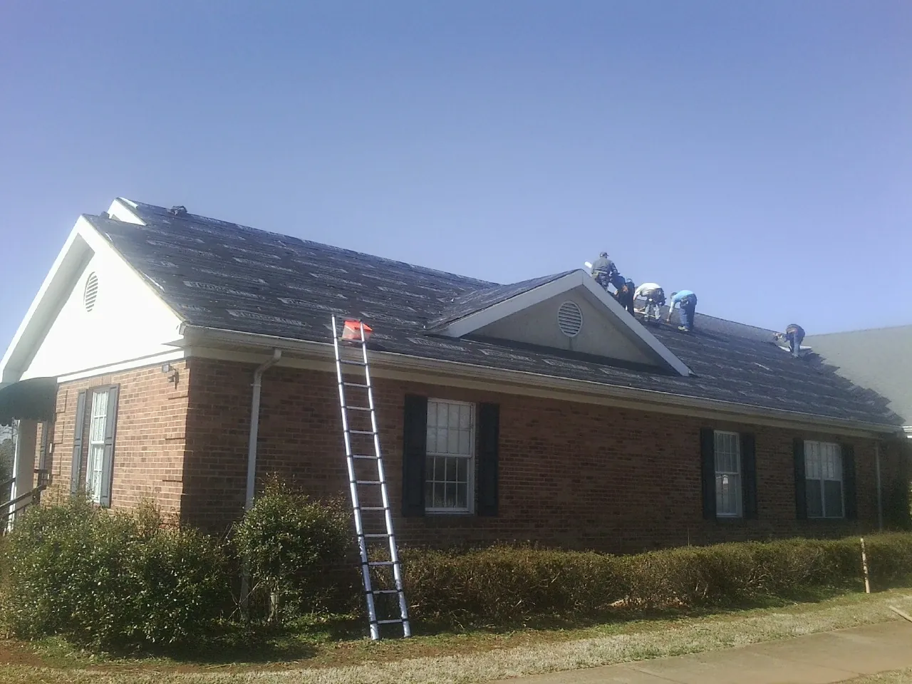 Crew tearing shingles off a brick ranch roof with a ladder set — Emergency Roof Repair work by our crew in Lakehead