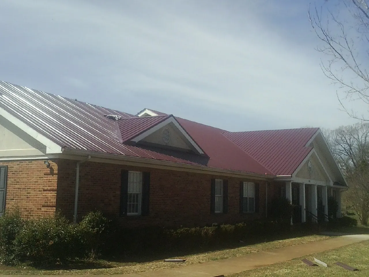 Red metal roof with gabled entries on a long brick building, from a Hail Damage Roof Repair job in Lakehead