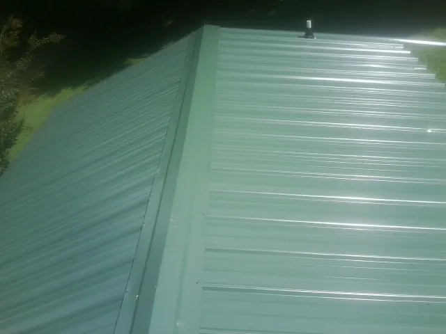 New green metal panels meeting at the ridge of a roof — Flat Roof Repair work by our crew in Lakehead