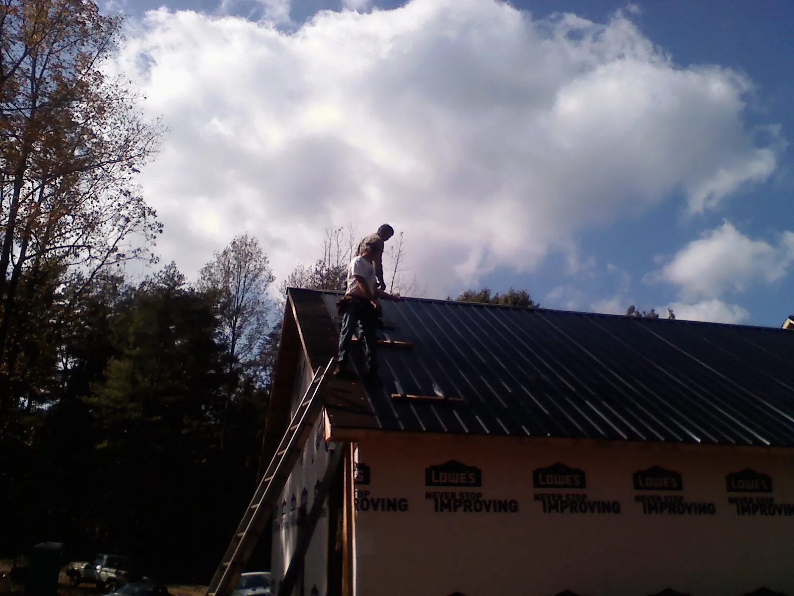 Roofer fastening dark metal panels high against a cloudy sky, from a Roof Inspection job in Lakehead
