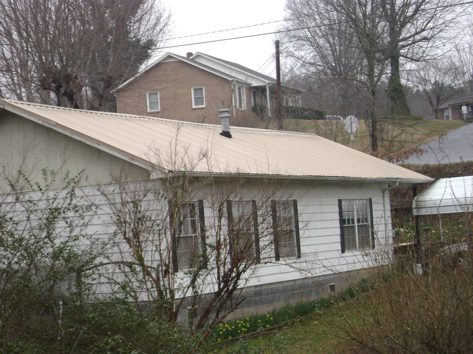 Tan metal roof on a white sided house set into a hillside — Commercial Roofing by Roofing Brothers in Lakehead