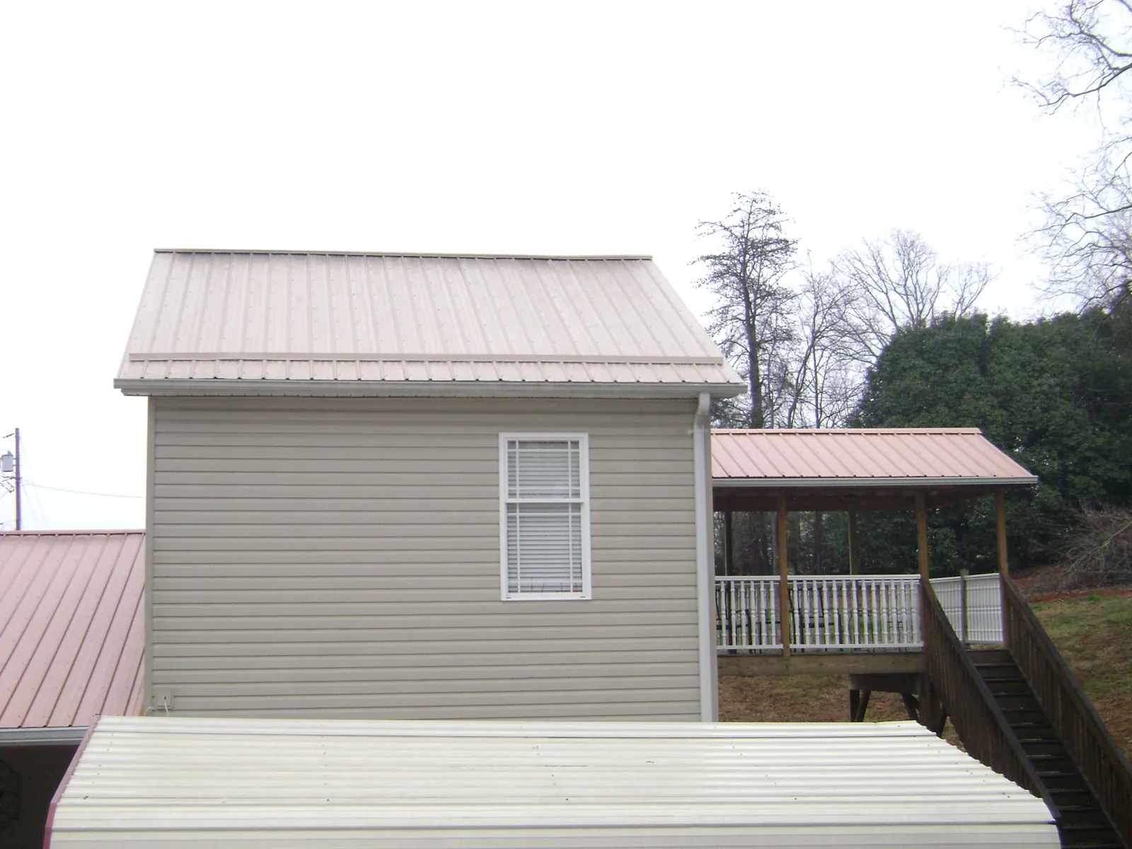 Tan metal roofs on a two story addition and attached porch, from a Roof Replacement job in Lakehead
